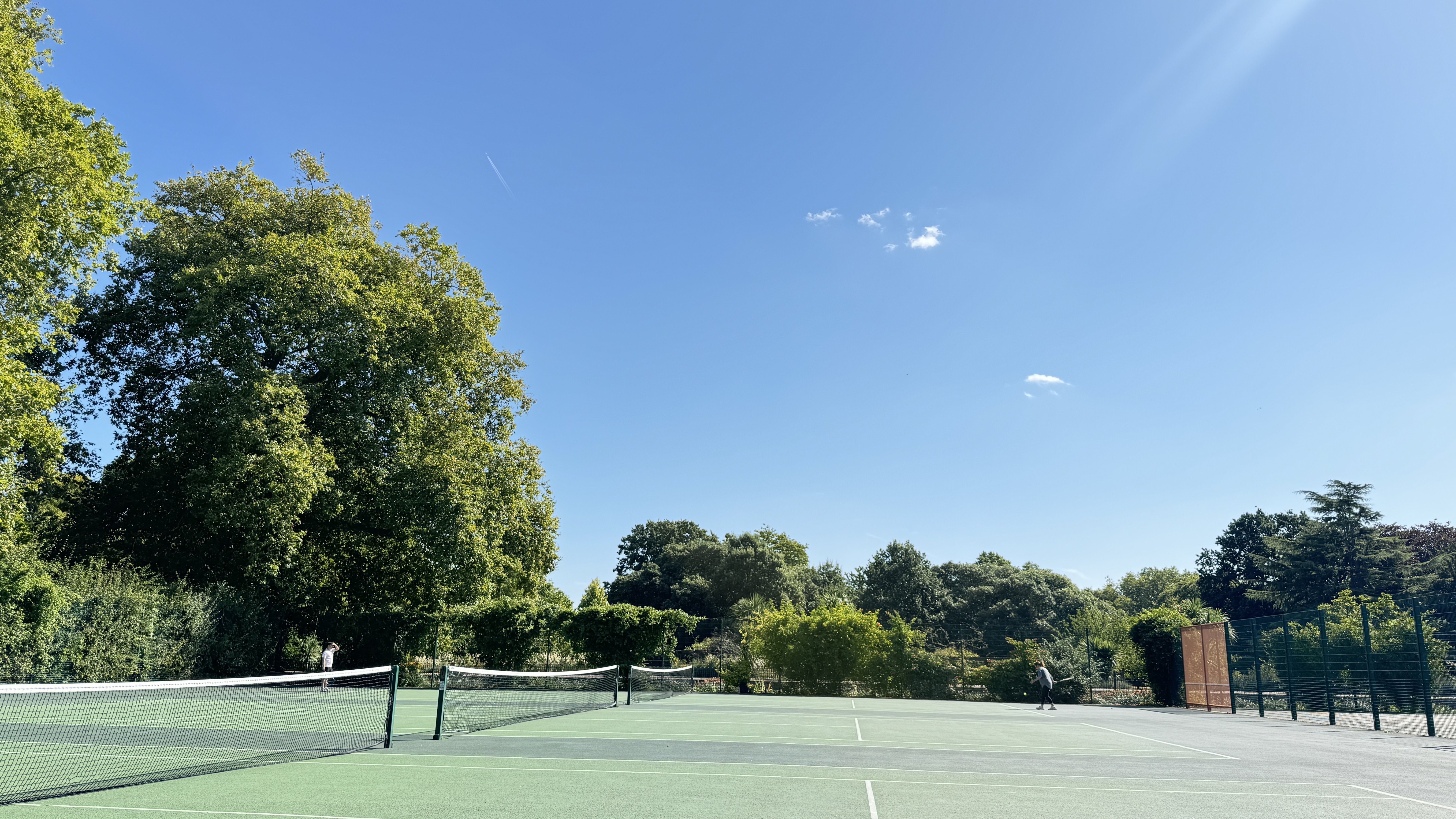 Wide tennis courts under a blue sky in West Ham Park